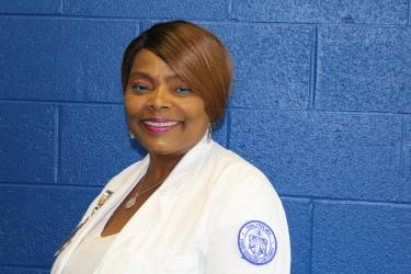 A Black woman stands in front of a blue brick wall and smiles.